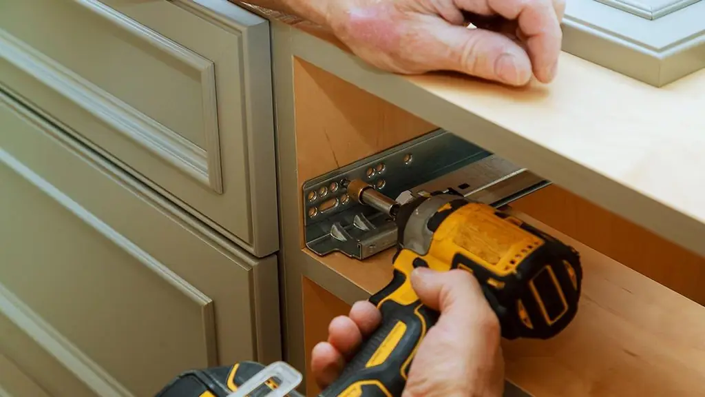 Close-up of a cabinet drawer slide being fitted with a cordless drill inside an open cabinet carcass